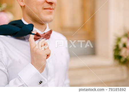 A man in a white shirt and with red bow tie holds a jacket thrown over his shoulder A man in a white shirt and with red bow tie holds a jacket thrown over his shoulder 78185892