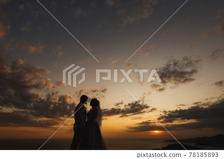 The bride and groom are embracing on the beach by the sea at sunset, silhouettes The bride and groom are embracing on the beach by the sea at sunset, silhouettes 78185893