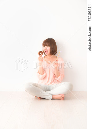 A young woman sitting cross-legged with a snack and a toothbrush in her hand A young woman sitting cross-legged with a snack and a toothbrush in her hand 78186214