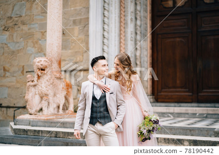 Bride with a bouquet of flowers hugs shoulders of smiling groom on the steps at the entrance to the Basilica of Santa Maria Maggiore in Rome Bride with a bouquet of flowers hugs shoulders of smiling groom on the steps at the entrance to the Basilica of Santa Maria Maggiore in Rome 78190442