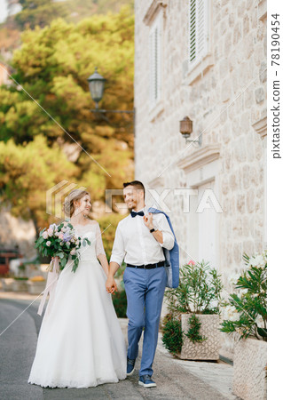 The bride and groom walk holding hands near a beautiful brick house in the old town of Perast The bride and groom walk holding hands near a beautiful brick house in the old town of Perast 78190454