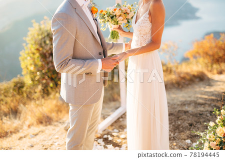 The bride and groom are standing on Mount Lovcen near the wedding arch and holding hands 78194445