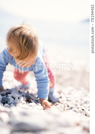 Cute baby is on all fours on a pebble beach with his head down. Close-up Cute baby is on all fours on a pebble beach with his head down. Close-up 78194482