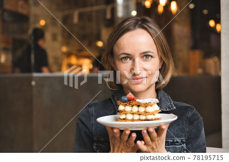 A beautiful caucasian woman holding and showing a plate with dessert in cafe A beautiful caucasian woman holding and showing a plate with dessert in cafe 78195715