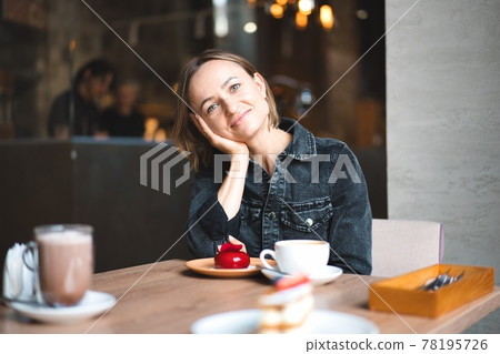 Portrait of a happy woman eating a piece of cake and drinking coffee while sitting at the table in a Portrait of a happy woman eating a piece of cake and drinking coffee while sitting at the table in a 78195726