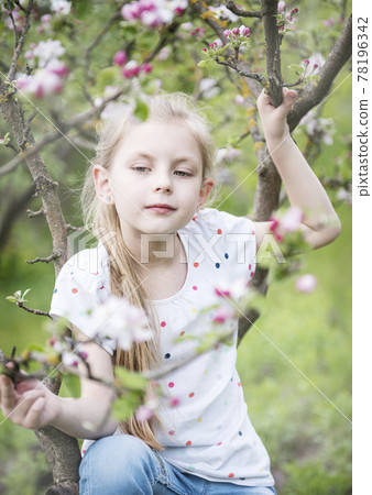 Little adorable girl sitting on blossoming tree 78196342