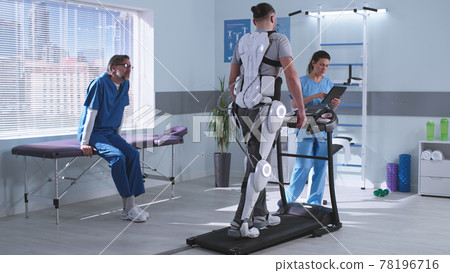 Male and female therapists controlling rehabilitation of man in exoskeleton 78196716