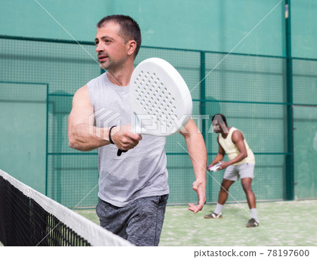 Male players playing padel in a padel court outdoor behind net 78197600