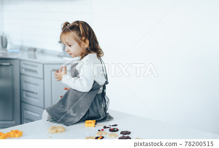 Little girl cooking sweet cookies, sitting on table 78200515