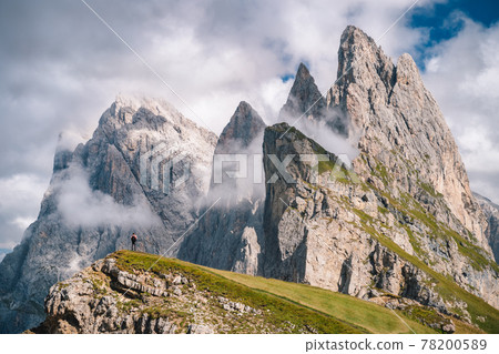 A man in front of epic Furchetta and Sass Rigais peaks in Seceda, Dolomites Alps, Odle mountain range, South Tyrol, Italy, Europe. Travel vacation concept A man in front of epic Furchetta and Sass Rigais peaks in Seceda, Dolomites Alps, Odle mountain range, South Tyrol, Italy, Europe. Travel vacation concept 78200589