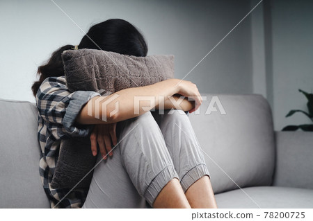 Unhappy lonely sad woman is sitting on the couch and hiding her face on a pillow, depression concept Unhappy lonely sad woman is sitting on the couch and hiding her face on a pillow, depression concept 78200725