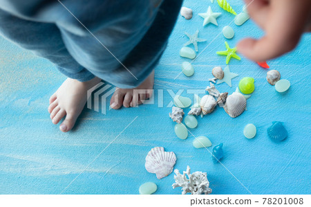 baby feet on Seashells summer background. Many different seashells, starfish on a background of blue paint strokes. Place for text. 78201008