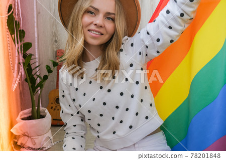 Young blonde millennial hippie woman with rainbow LGBTQ flag at home balcony. Peace and freedom the symbol of LGBT, spending and sharing loving time. Support LGBTQ community. Young blonde millennial hippie woman with rainbow LGBTQ flag at home balcony. Peace and freedom the symbol of LGBT, spending and sharing loving time. Support LGBTQ community. 78201848