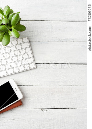 Office desktop with computer keyboard, smart phone, notebook and green plant on white wooden table. Business background Office desktop with computer keyboard, smart phone, notebook and green plant on white wooden table. Business background 78206986