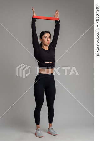 Girl stretching resistance band on arms overhead on grey background Girl stretching resistance band on arms overhead on grey background 78207987