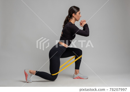 Girl doing lunge with resistance band on grey background Girl doing lunge with resistance band on grey background 78207997