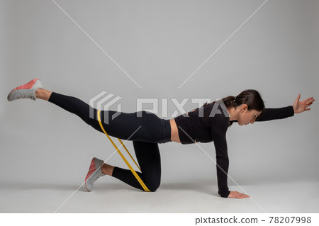 Woman doing Dandayamana Bharmanasana with resistance band on grey background 78207998