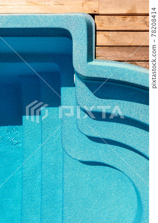 New modern fiberglass plastic swimming pool entrance step with clean fresh refreshing blue water on bright hot summer day at yard or resort hotel spa area. Wooden flooring deck of teak or larch board New modern fiberglass plastic swimming pool entrance step with clean fresh refreshing blue water on bright hot summer day at yard or resort hotel spa area. Wooden flooring deck of teak or larch board 78208414