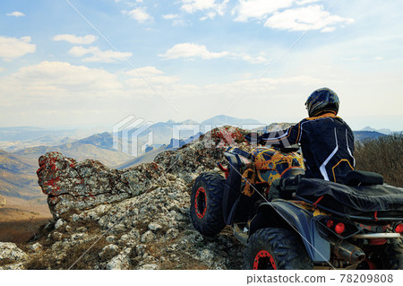 Man in helmet sitting on ATV quad bike in mountains 78209808