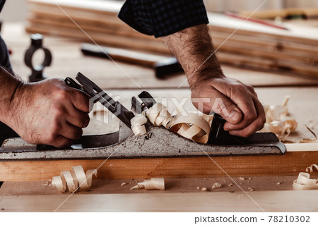 Carpenter's hands planing a plank of wood with a hand plane Carpenter's hands planing a plank of wood with a hand plane 78210302
