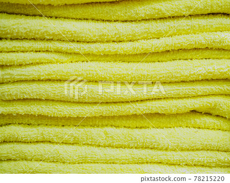Yellow terry identical towels are stacked in a stack. Background texture. Full-screen photos 78215220