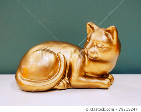 The golden figurine of the cat lies on the shelf against the background of the gray blue wall 78215247