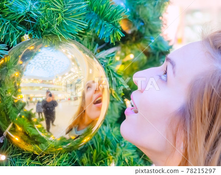 The girl's face looking up and her reflection in a golden ball hanging on the tree The girl's face looking up and her reflection in a golden ball hanging on the tree 78215297
