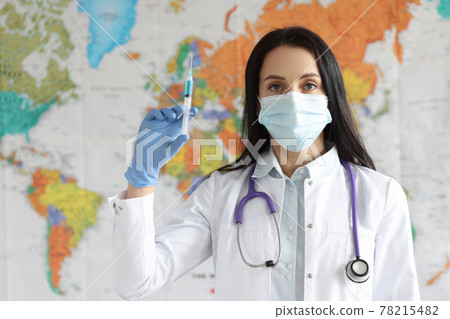 Woman doctor in protective medical mask holds syringe with vaccine on background of world map Woman doctor in protective medical mask holds syringe with vaccine on background of world map 78215482