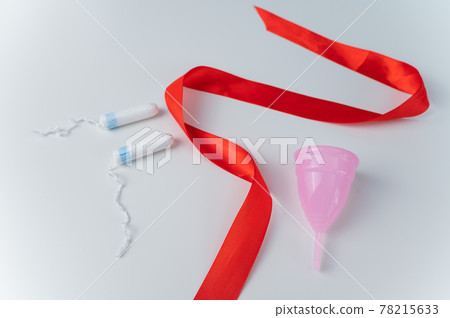 Tampon, pink menstrual cup and red satin ribbon on a white background. Means of intimate hygiene of a woman during mentruation Tampon, pink menstrual cup and red satin ribbon on a white background. Means of intimate hygiene of a woman during mentruation 78215633