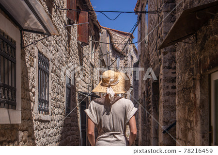 Beautiful blonde young female traveler wearing straw sun hat sightseeing and enjoying summer vacation in an old traditional costal town at Adriatic cost, Croatia Beautiful blonde young female traveler wearing straw sun hat sightseeing and enjoying summer vacation in an old traditional costal town at Adriatic cost, Croatia 78216459