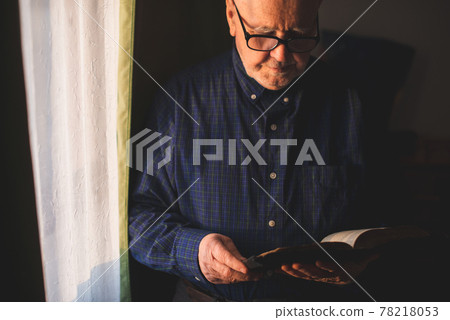 Elderly man stand next to window and reading Bible Elderly man stand next to window and reading Bible 78218053