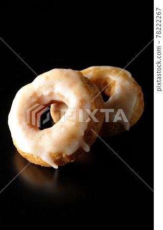 在黑色背景上拍攝的兩個重疊的蜂蜜釉甜甜圈 在黑色背景上拍攝的兩個重疊的蜂蜜釉甜甜圈 78222267