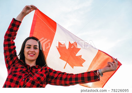 Young millennial brunette woman holding The National Flag of Canada. Canadian Flag or the Maple Leaf. Tourist traveler or patriotism. Immigrant in a free country. Independence day 1th july Young millennial brunette woman holding The National Flag of Canada. Canadian Flag or the Maple Leaf. Tourist traveler or patriotism. Immigrant in a free country. Independence day 1th july 78226095
