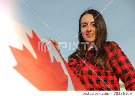 Young millennial brunette woman holding The National Flag of Canada. Canadian Flag or the Maple Leaf. Tourist traveler or patriotism. Immigrant in a free country. Independence day 1th july 78226109