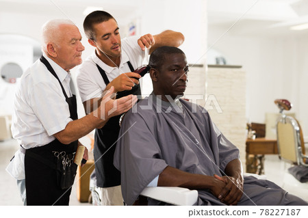 Aged barber teaching apprentice to male haircut 78227187