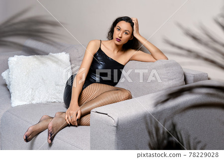 Barefoot african american woman sits with legs tucked on couch Barefoot african american woman sits with legs tucked on couch 78229028