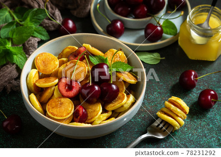Trendy home breakfast. Mini pancakes, honey and cherries on a stone table. Trendy home breakfast. Mini pancakes, honey and cherries on a stone table. 78231292