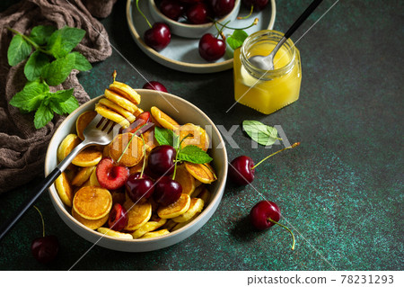 Trendy home breakfast. Mini pancakes, honey and cherries on a stone table. Copy space. Trendy home breakfast. Mini pancakes, honey and cherries on a stone table. Copy space. 78231293