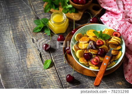 Tiny pancakes breakfast. Mini pancakes with cherries and honey on rustic wooden table. Copy space. Tiny pancakes breakfast. Mini pancakes with cherries and honey on rustic wooden table. Copy space. 78231298