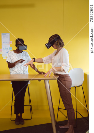 Diverse businesswomen standing at desk using vr headset at work Diverse businesswomen standing at desk using vr headset at work 78232691