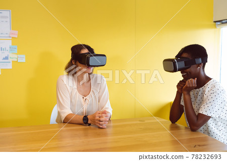 Diverse businesswomen sitting at desk using vr headset at work Diverse businesswomen sitting at desk using vr headset at work 78232693