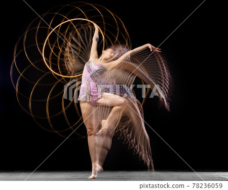 Portrait of young girl rhythmic gymnast in motion and action isolated in mixed light on dark background. 78236059