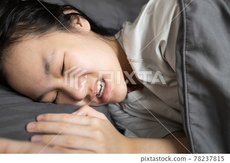 Asian lady girl suffering from bruxism while lying in bed at night,female grinding of the teeth during sleep,teeth clenching,sleep disorders,oral health problems,dental care,sleep bruxism concept 78237815