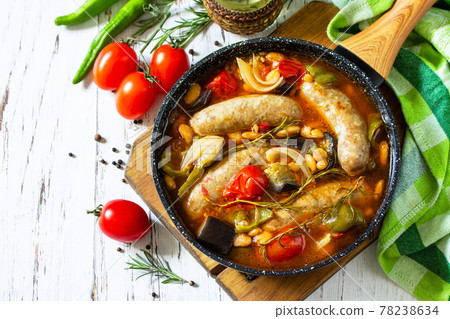 Stew of beans, vegetables and smoked sausages with tomato sauce in the pan on wooden table. Copy space. Stew of beans, vegetables and smoked sausages with tomato sauce in the pan on wooden table. Copy space. 78238634