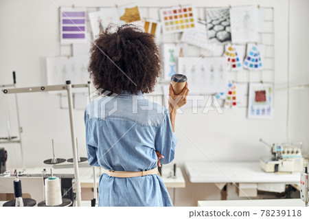 African-American woman fashion designer near sewing machines in workshop backside view 78239118