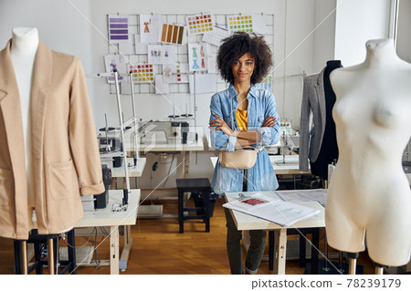 Positive African-American woman tailor stands at table with drawings in sewing workshop 78239179