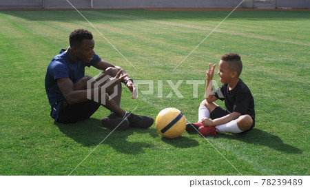 Diverse trainer and boy talking on football pitch 78239489