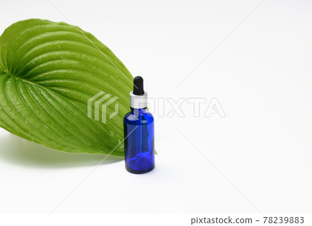 blue glass transparent bottle with a pipette on the background of a green leaf 78239883