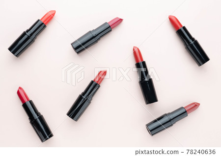 Red lipsticks of different shades  in black tube package on beige background. Makeup and cosmetics concept. Flat layout. 78240636
