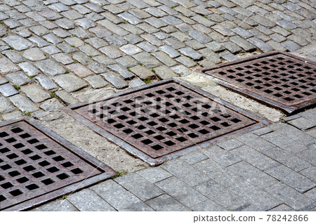 drainage system of urban infrastructure with an iron grating of the hatch of the stormwater system of the sidewalk from granite tiles near the road from the paving stones, nobody. 78242866